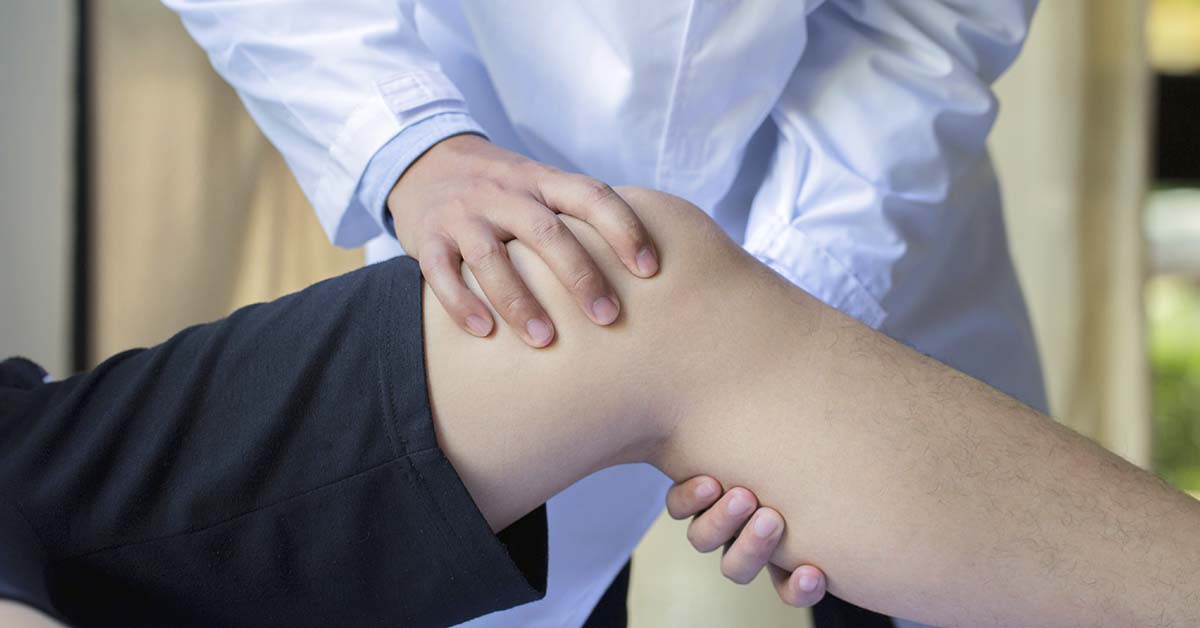 Médico com as mãos no joelho do paciente deitado
